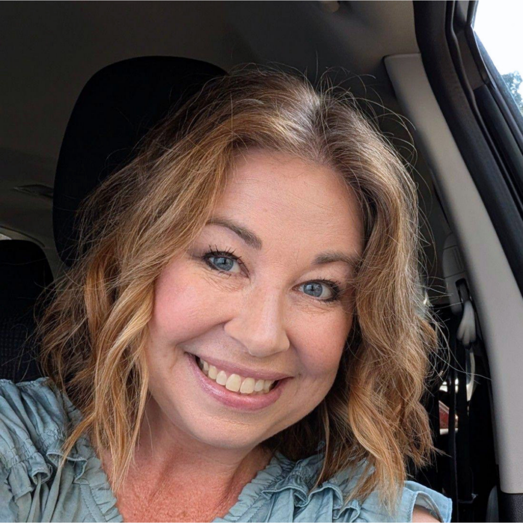 Smiling woman with shoulder-length blonde hair sitting in a vehicle.